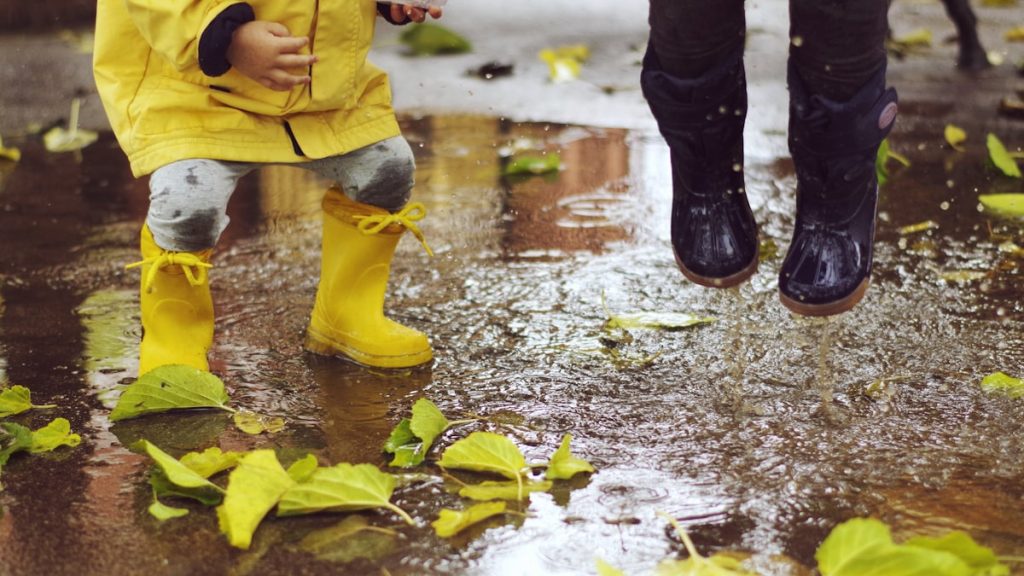 Enfant en bottes de pluie jaunes sautant dans une flaque à côté d'une paire de bottes plus grande